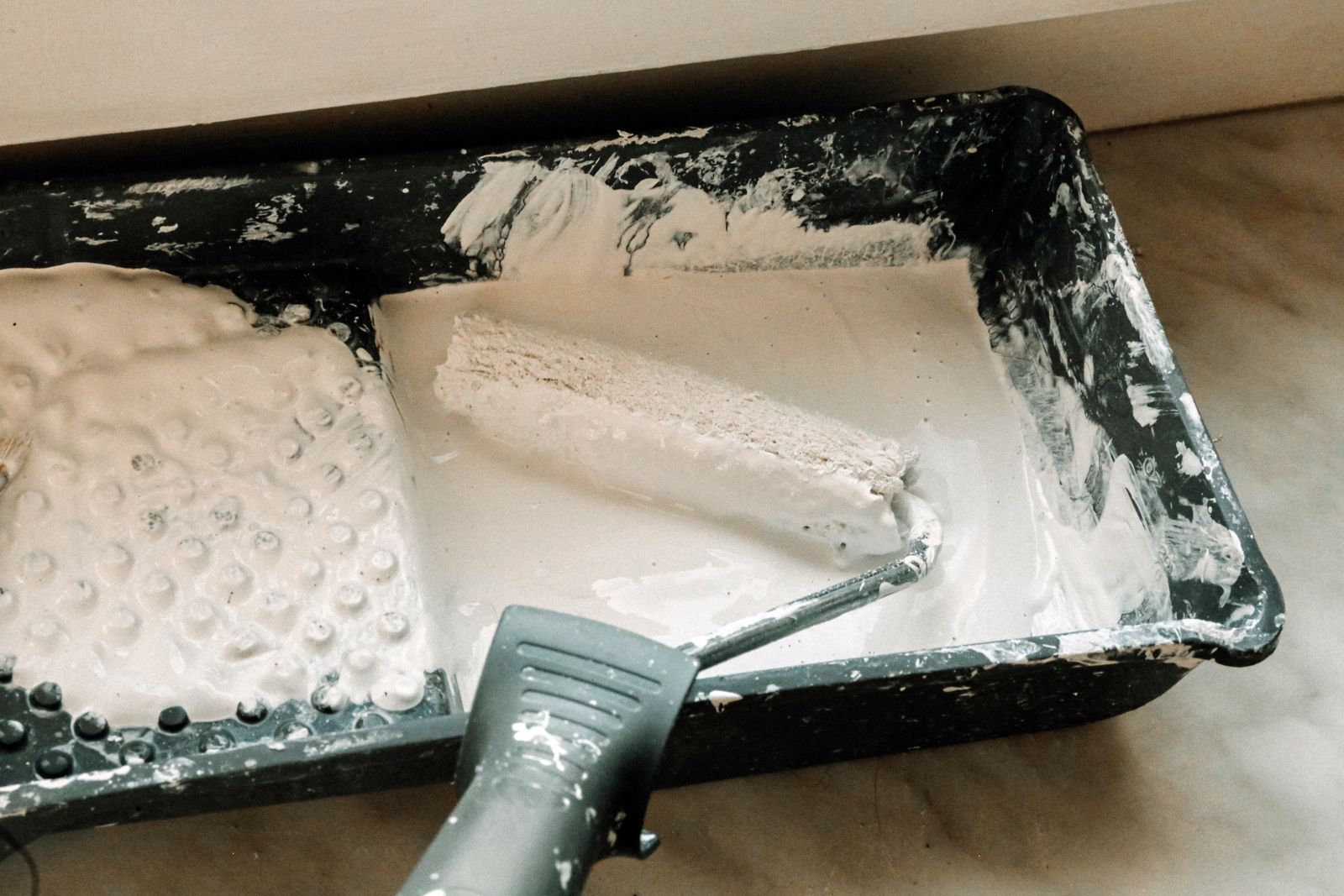 Verfroller wordt gedoopt in witte verf in een verfbak