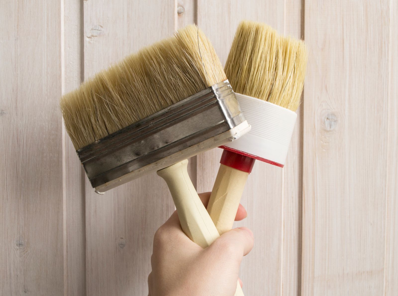 Hand houdt twee kwasten vast voor een houten ondergrond