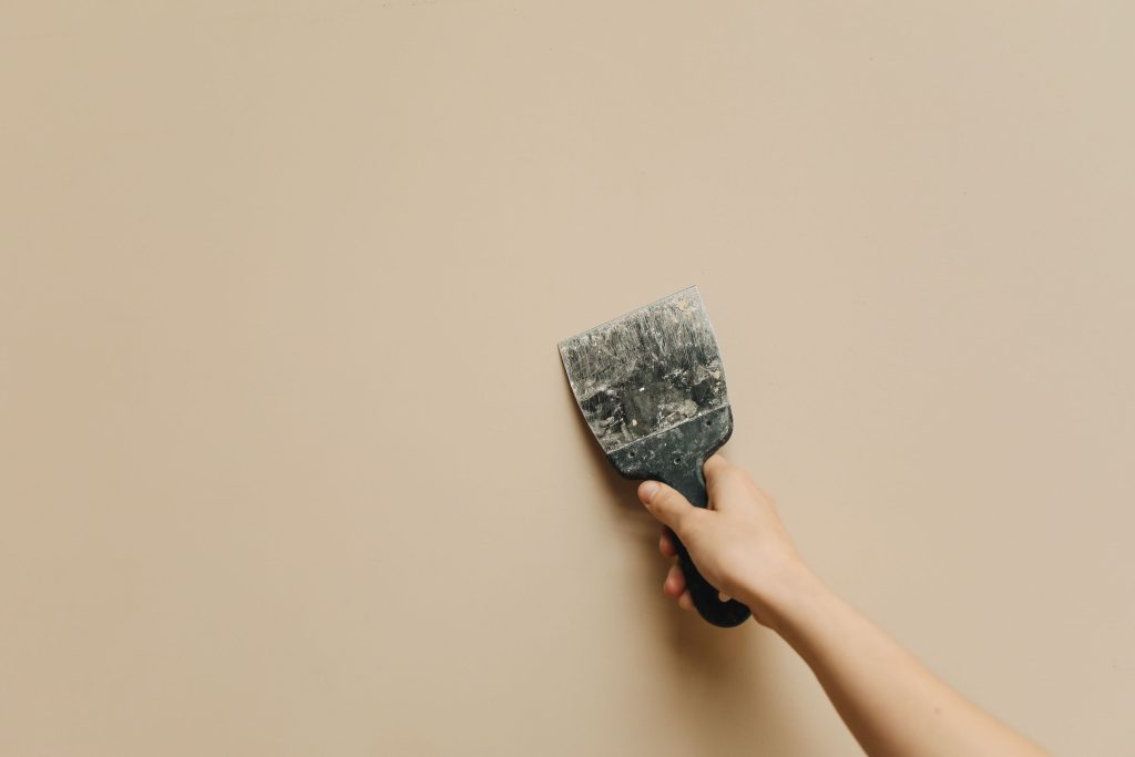 Hand houdt een spatel tegen een kale muur tijdens verbouwing