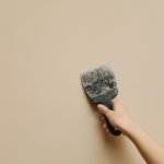 Hand houdt een spatel tegen een kale muur tijdens verbouwing