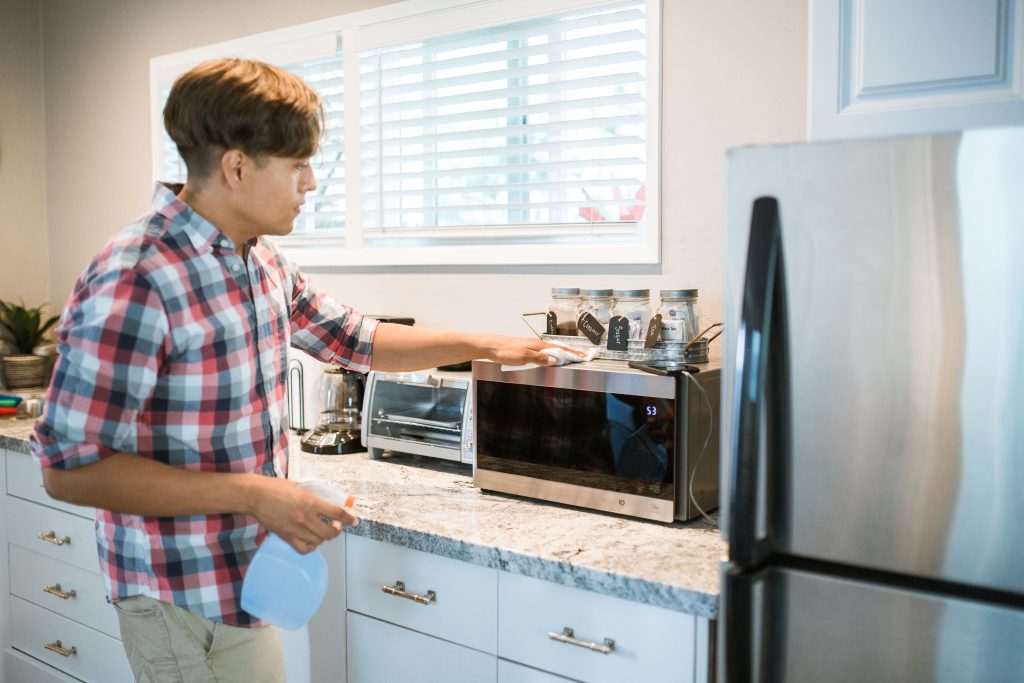 Persoon reinigt keukenapparaat met spuitfles en poetsdoek