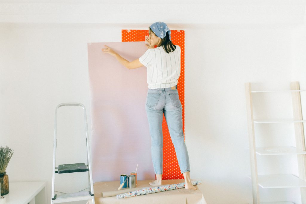 Vrouw brengt vlies-behang aan op een muur tijdens verbouwing