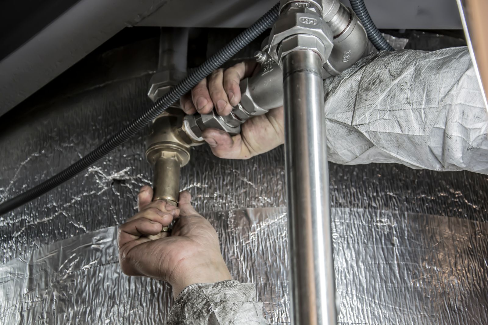 Handen van een monteur die metalen leidingen onder een aanrecht bevestigen