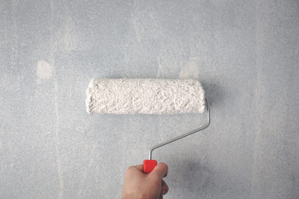Hand met verfroller brengt witte verf aan op muur