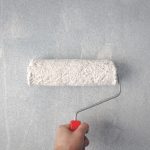 Hand met verfroller brengt witte verf aan op muur