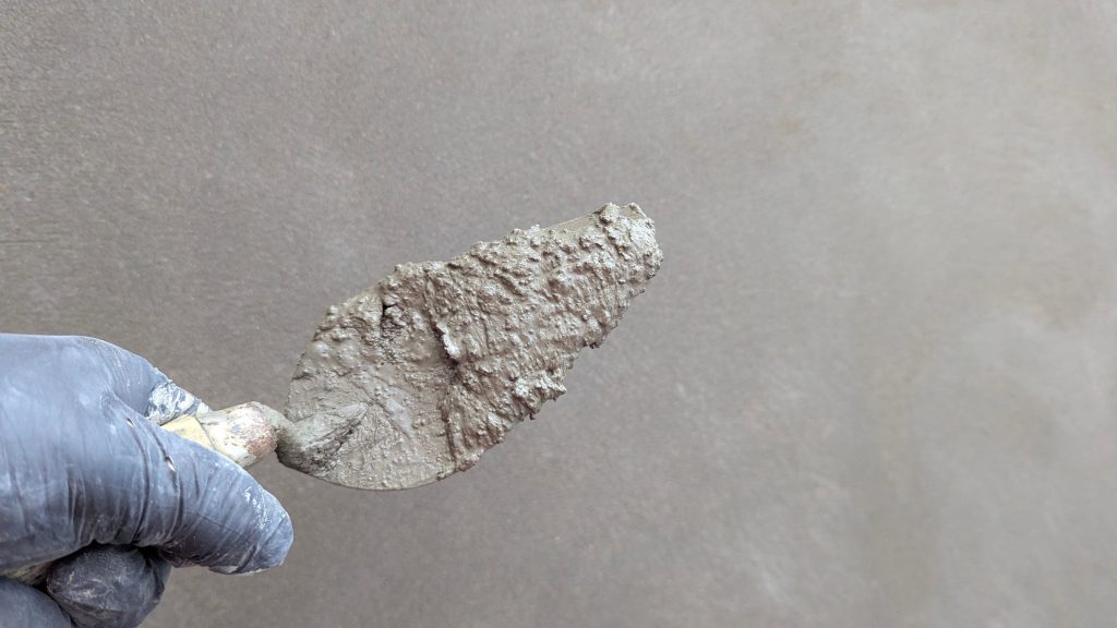 Hand met troffel brengt stucwerk aan op een muur