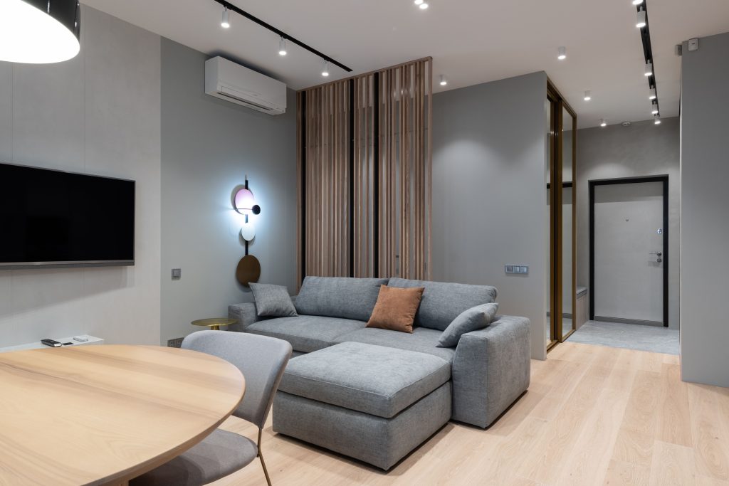Woonkamer met grijze bank en airco-unit aan de wand